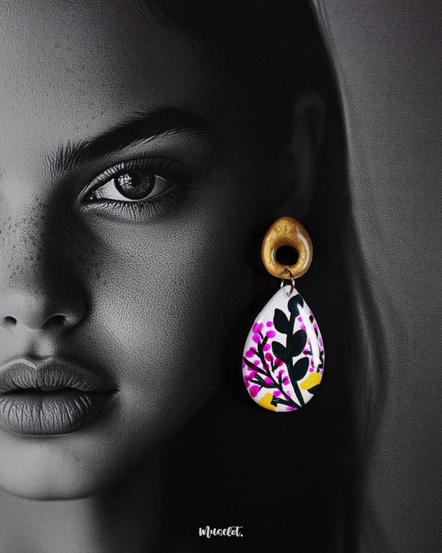 A close-up of a model wearing the Raushanbahaar handmade floral drop earrings, showcasing the teardrop design with vivid hand-painted pink and yellow flowers and lush green leaves, highlighting their detailed artistry and bold statement charm — Muselot.