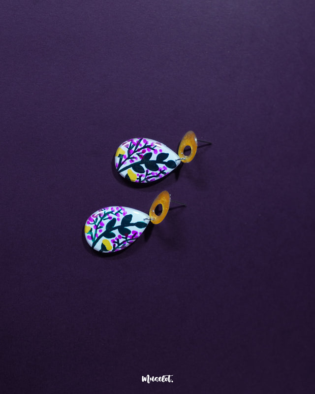 Raushanbahaar floral drop earrings laid against a soft neutral background, featuring a teardrop silhouette with delicate pink and yellow floral artwork and leafy details, highlighting the lively hand-painted charm and showcasing the beauty of handcrafted accessories — Muselot.