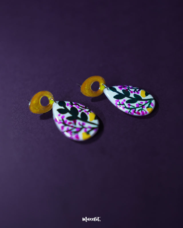 A zoomed-in view of Raushanbahaar floral drop earrings showing the intricate hand-painted pink and yellow blossoms with green leafy accents on a teardrop base, highlighting the detailed craftsmanship and showcasing the graceful charm of folk-inspired design — Muselot.