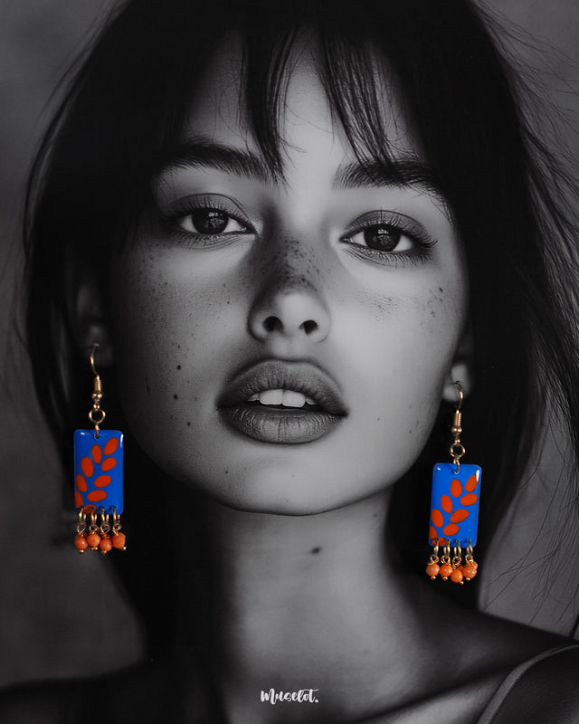 A model wears the Sandhyaraag boho drop earrings, highlighting the vivid blue base with bold orange petal motifs, showcasing their artsy design and vibrant charm — Muselot.