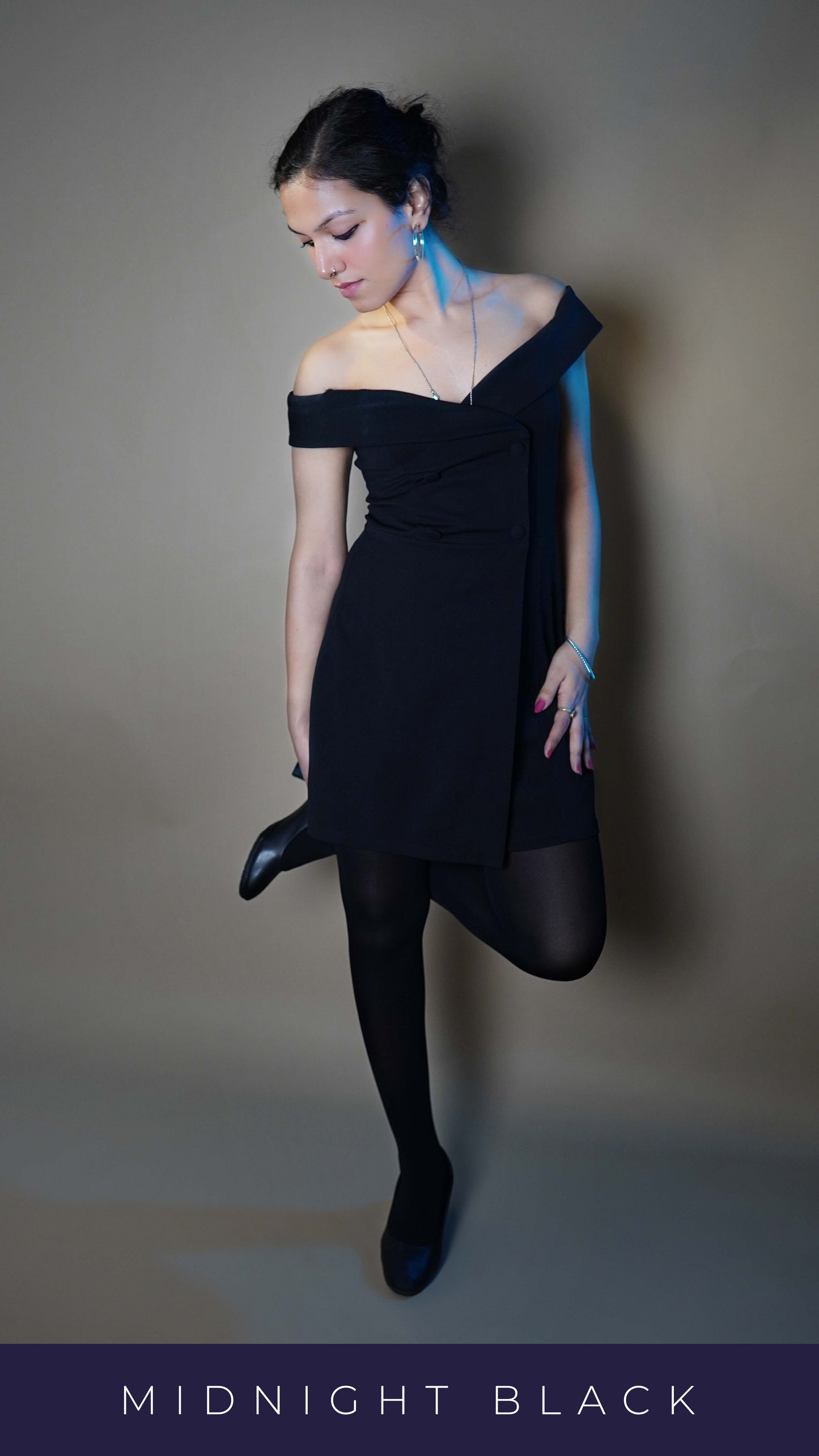 A woman wearing women's black semi opaque tights, posing with her leg pulled behind her other leg and hand touching her ankle as she look down at it, showcasing a sassy elegant look-Muselot