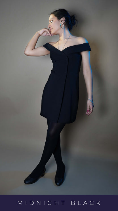 A woman wearing black moisture wicking pantyhose for women, posing with her hand on her chin as she looks sideways with the other hand hanging at her side and legs crossed, showcasing a modish perfect look-Muselot