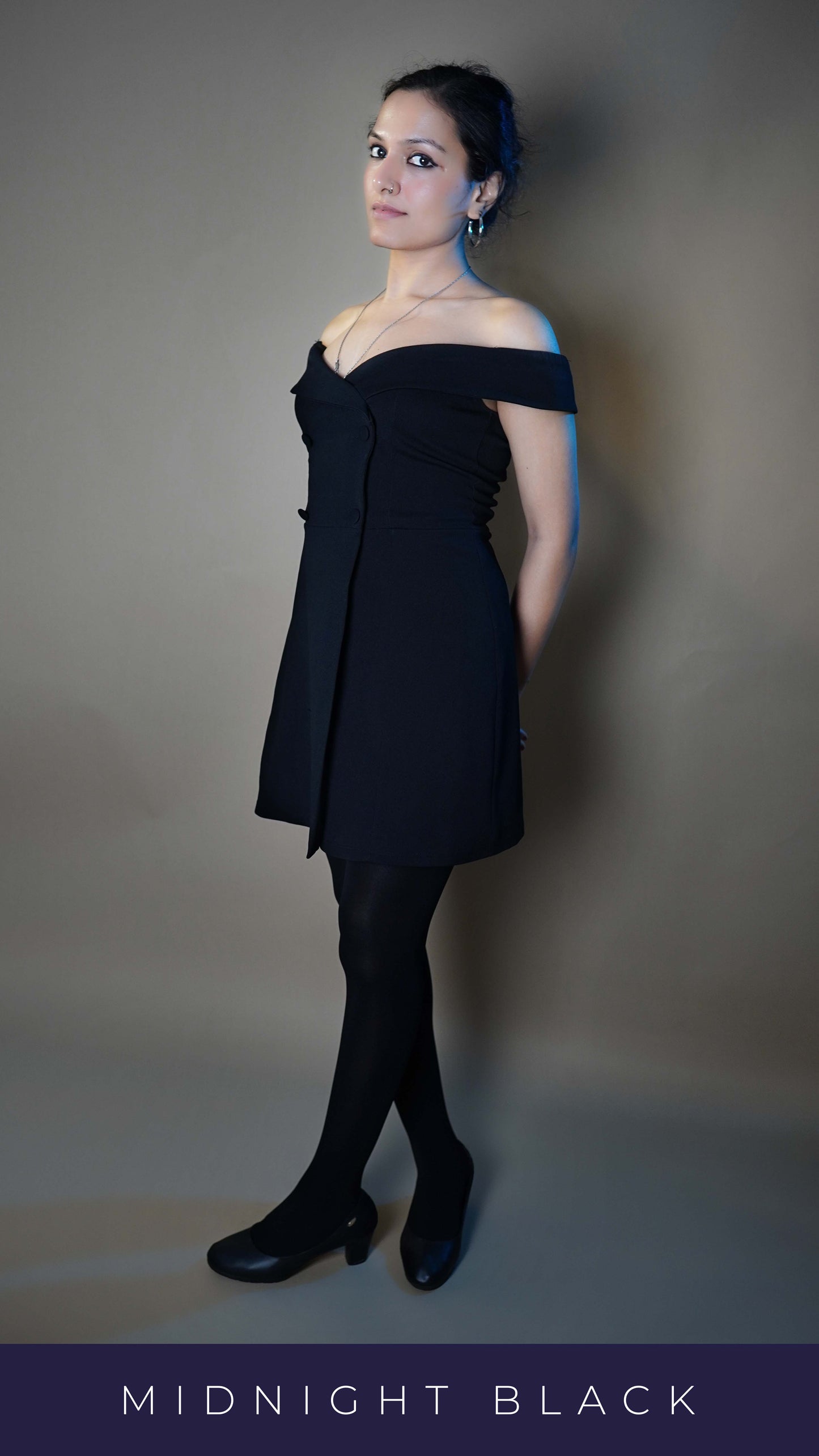 A model wearing black stocking that are semi opaque posing with her hands tied at her back as she leans upon the wall behind her and look sideways, highlighting an in vogue fashionable look-Muselot