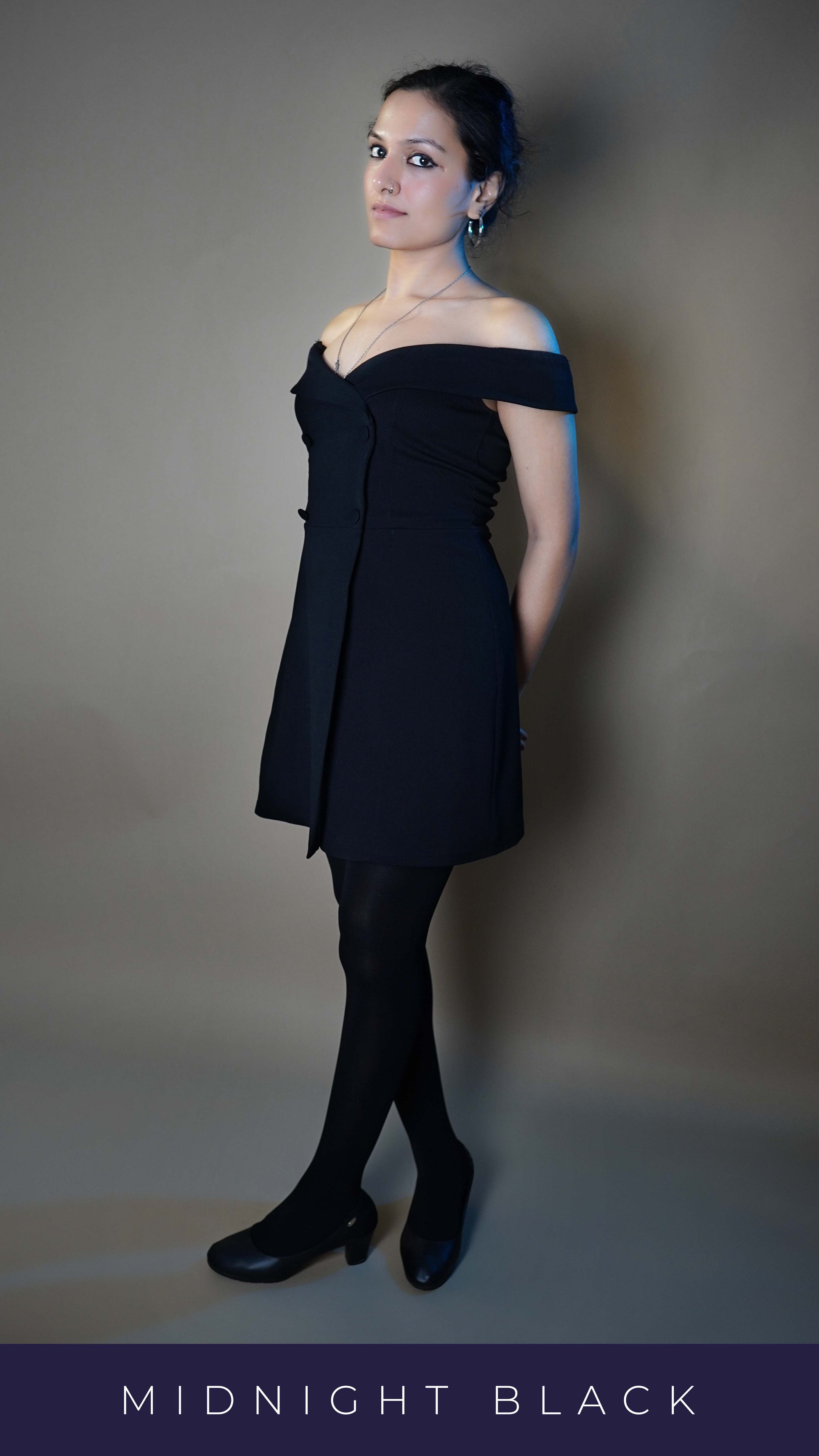 A model wearing black stocking that are semi opaque posing with her hands tied at her back as she leans upon the wall behind her and look sideways, highlighting an in vogue fashionable look-Muselot