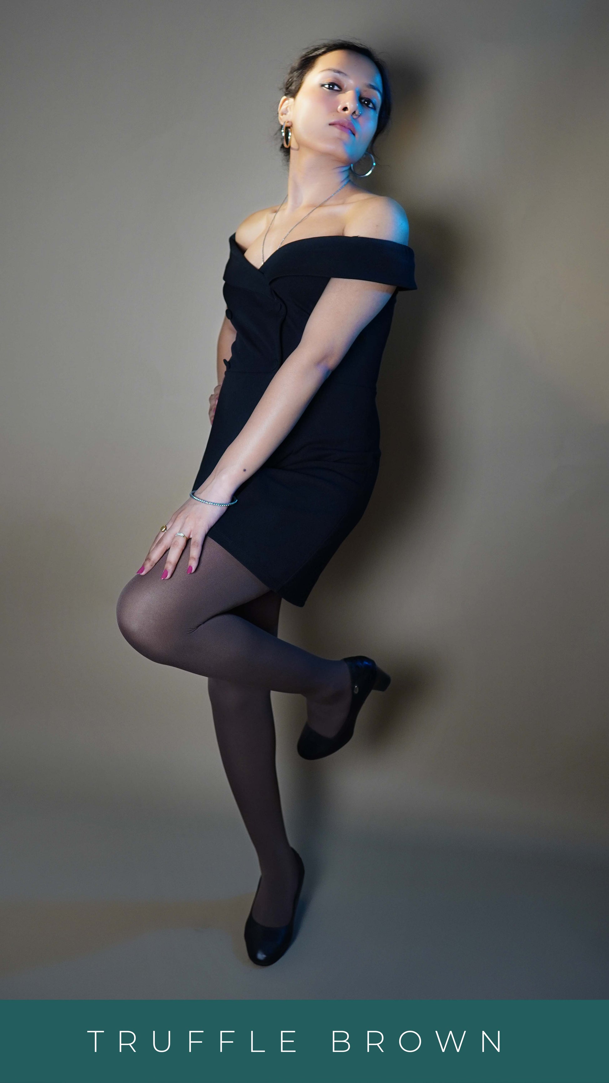 A model wearing tear resistant dark brown tights for females, posing with her foot on the wall behind her and a hand stretched to lie on her thigh as she stands slightly sideways, highlighting the classy modish look-Muselot