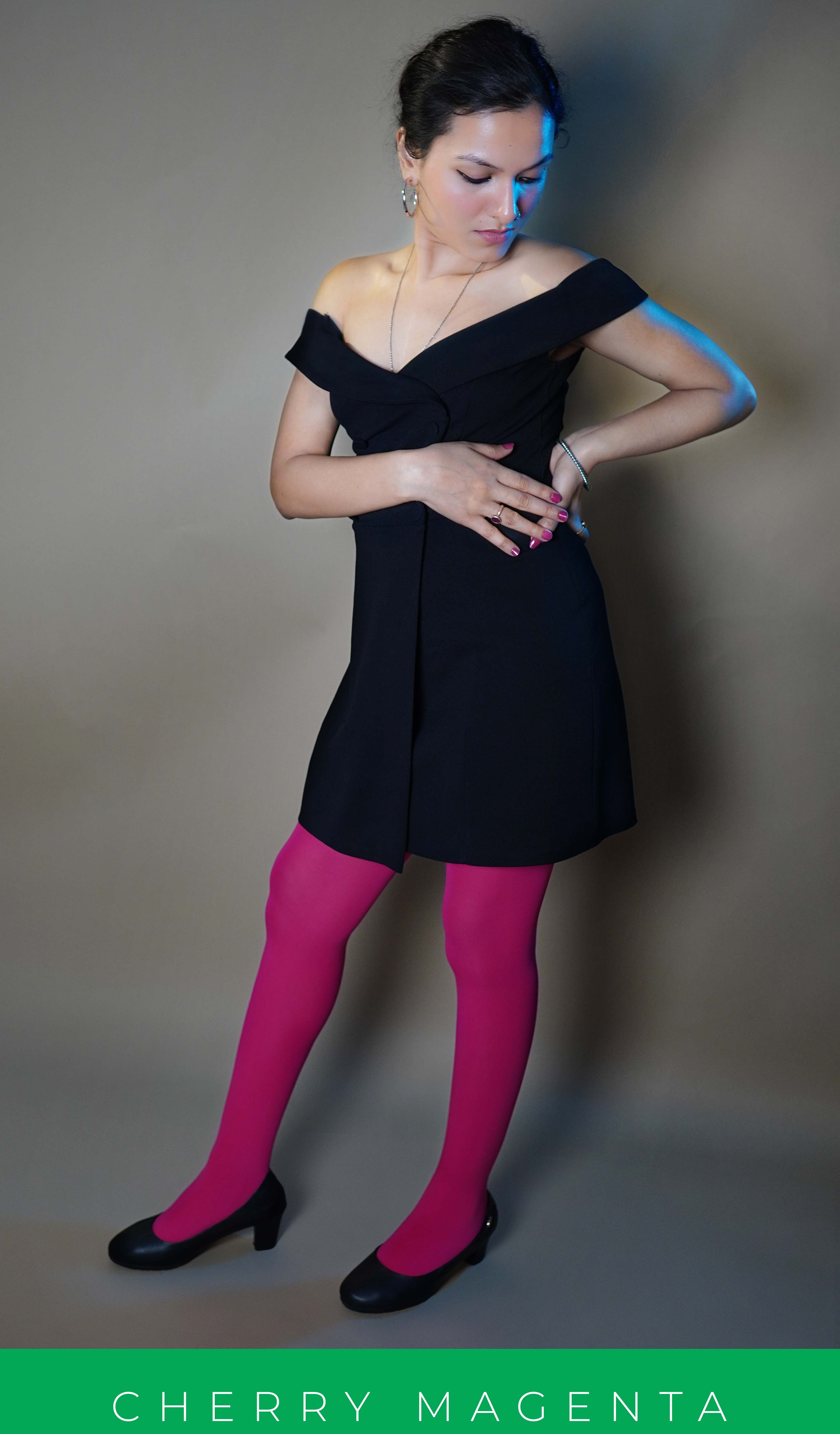 A woman wearing hot pink women's tights paired with a black dress, posing with her hand on her waist as the other touches its thumb, highlighting a smooth perfect fit-Muselot