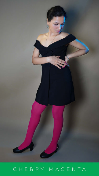 A woman wearing hot pink women's tights paired with a black dress, posing with her hand on her waist as the other touches its thumb, highlighting a smooth perfect fit-Muselot