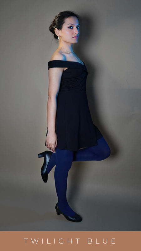 A woman wearing navy blue colored semi opaque stocking, posing with her leg pulled upward as she stands sideways, highlighting the durable tear resistant material-Muselot