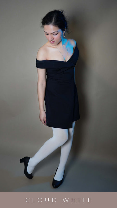 A woman wearing semi opaque white tights for girls, posing with her leg bent backwards as she looks down at it, highlighting the opaque smooth texture-Muselot