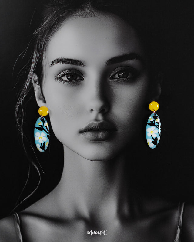 A woman wears the oval-shaped Shaamgul floral drop earrings against a deep purple background, highlighting the sky-blue base, white daisies, black leaves, and yellow stud—beautifully showcasing their handmade charm and standout design — Muselot.