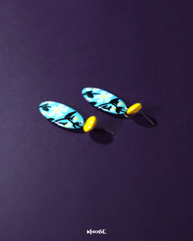 Shaamgul drop earrings placed against an oval-shaped purple background, highlighting the intricate floral details and elegant hanging beads in a handcrafted design — Muselot.