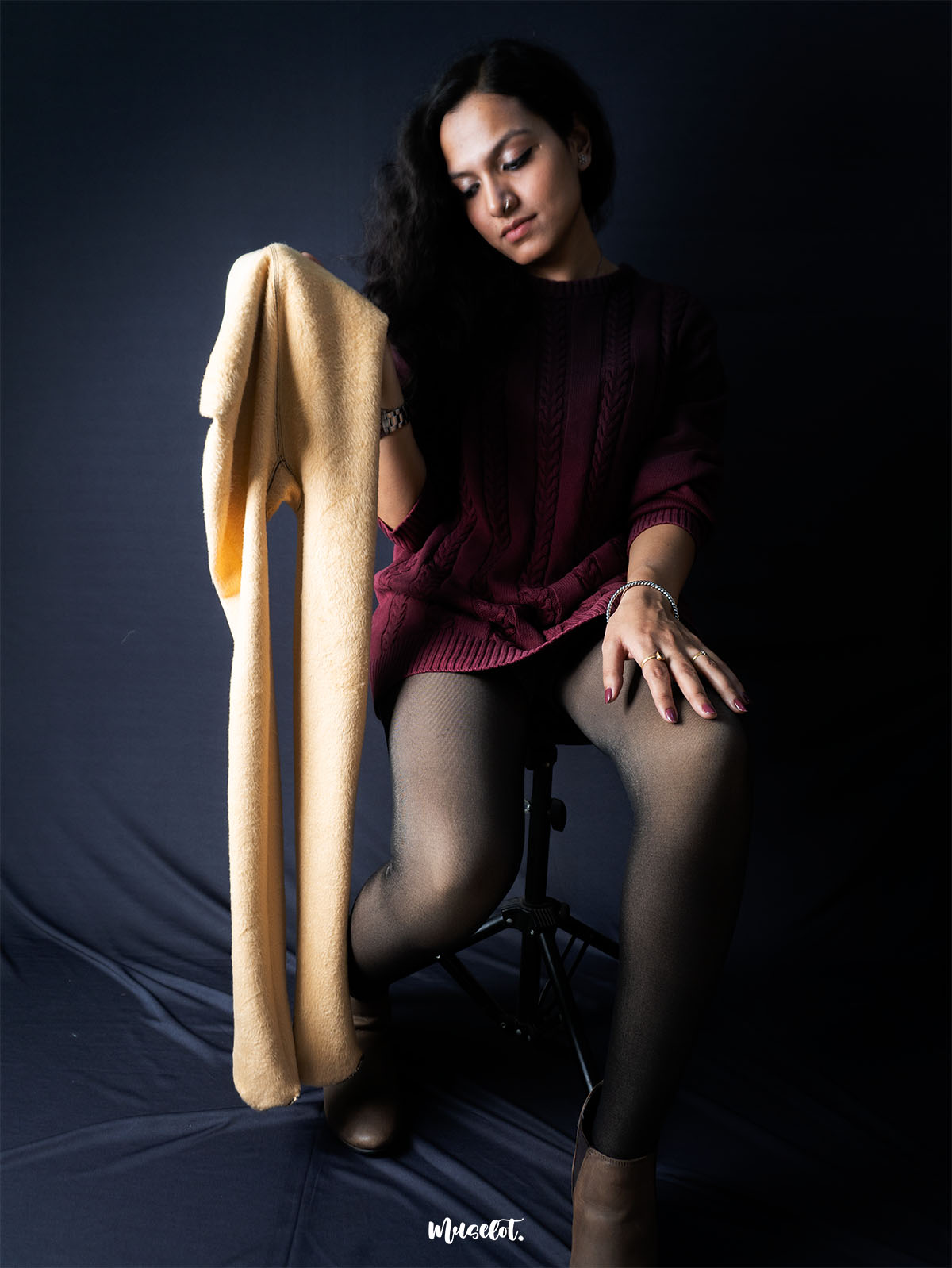 A model sitting on chair holding a sheer fur stockings, showcasing the stretchability and durability of the stockings-Muselot