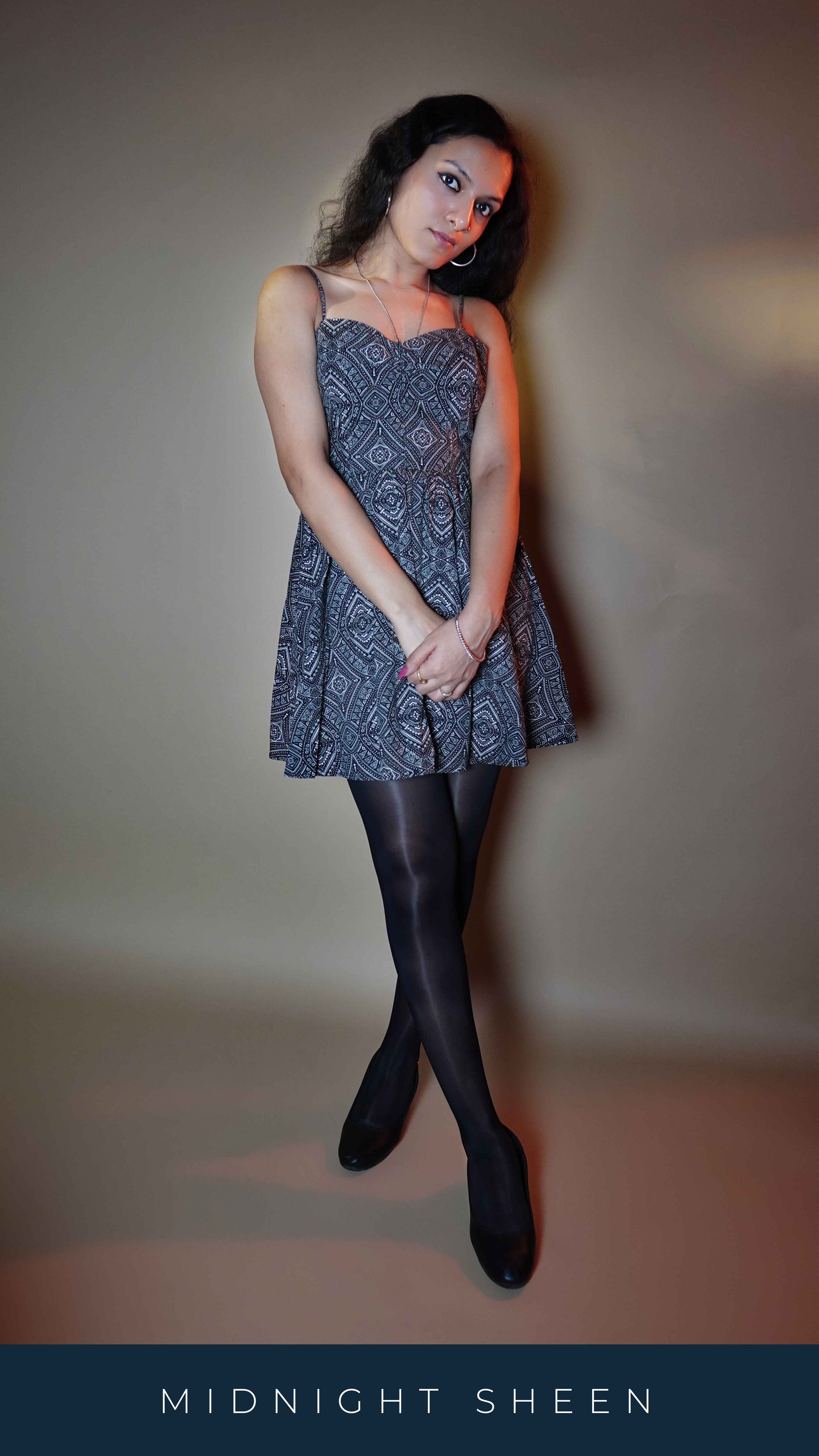 A model posing with her hand grabbing the other at her front as she looks gently at the camera with her head slightly bend downwards, wearing a silken touch black sheer pantyhose, showcasing the trendy snug fit-Muselot