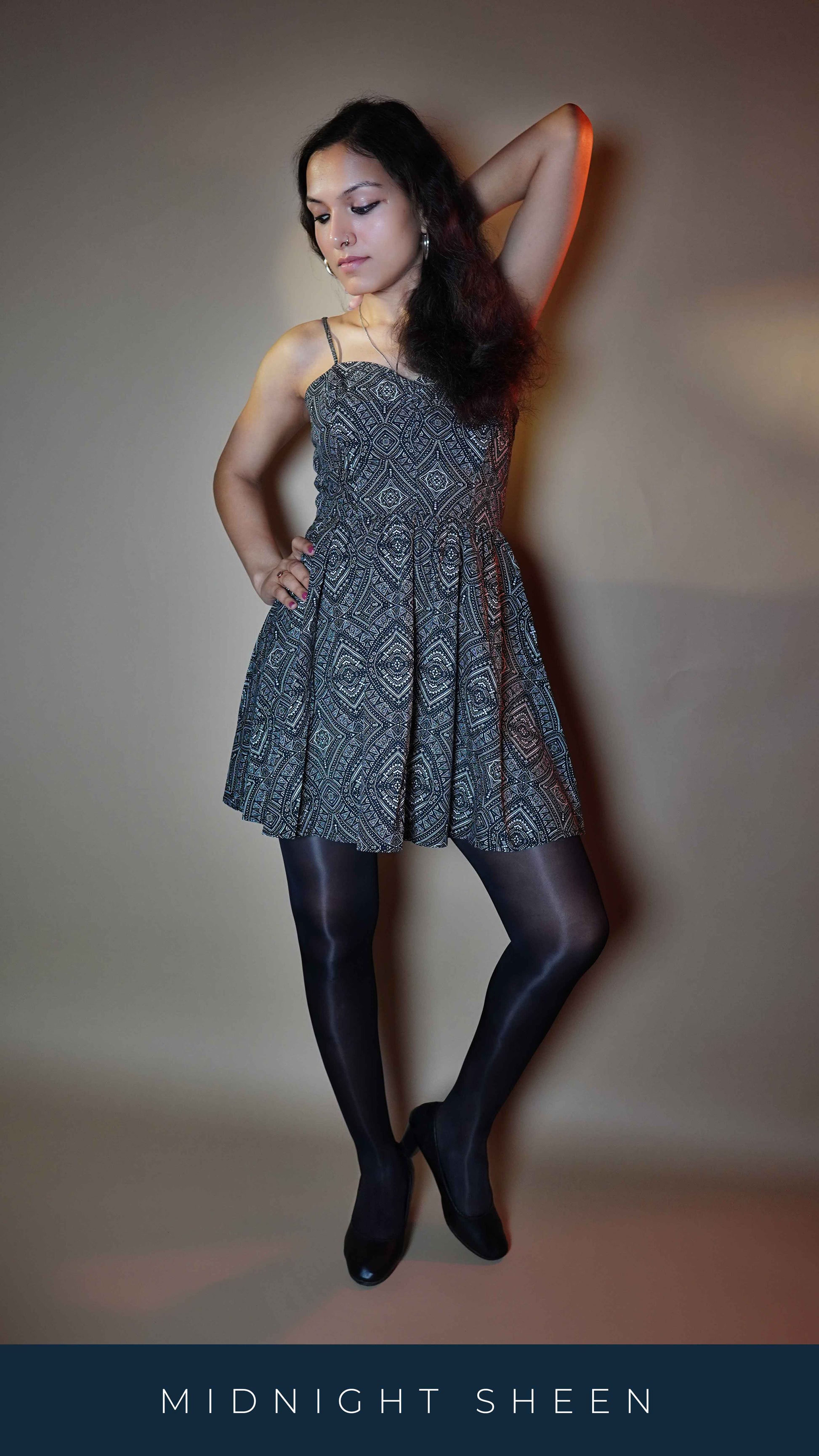 A woman wearing transparent breathable black sheer tights, posing with her hand up behind her head and other on her waist as she looks sideways, highlighting the modern in vogue look-Muselot