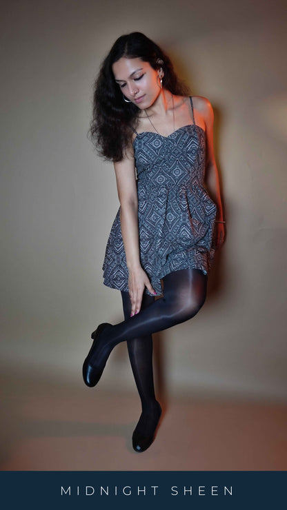 A model wearing ultra sheer black durable pantyhose, posing with her hand touching her leg as she pulls it up to her knee length, showcasing the smooth transparent material-Muselot