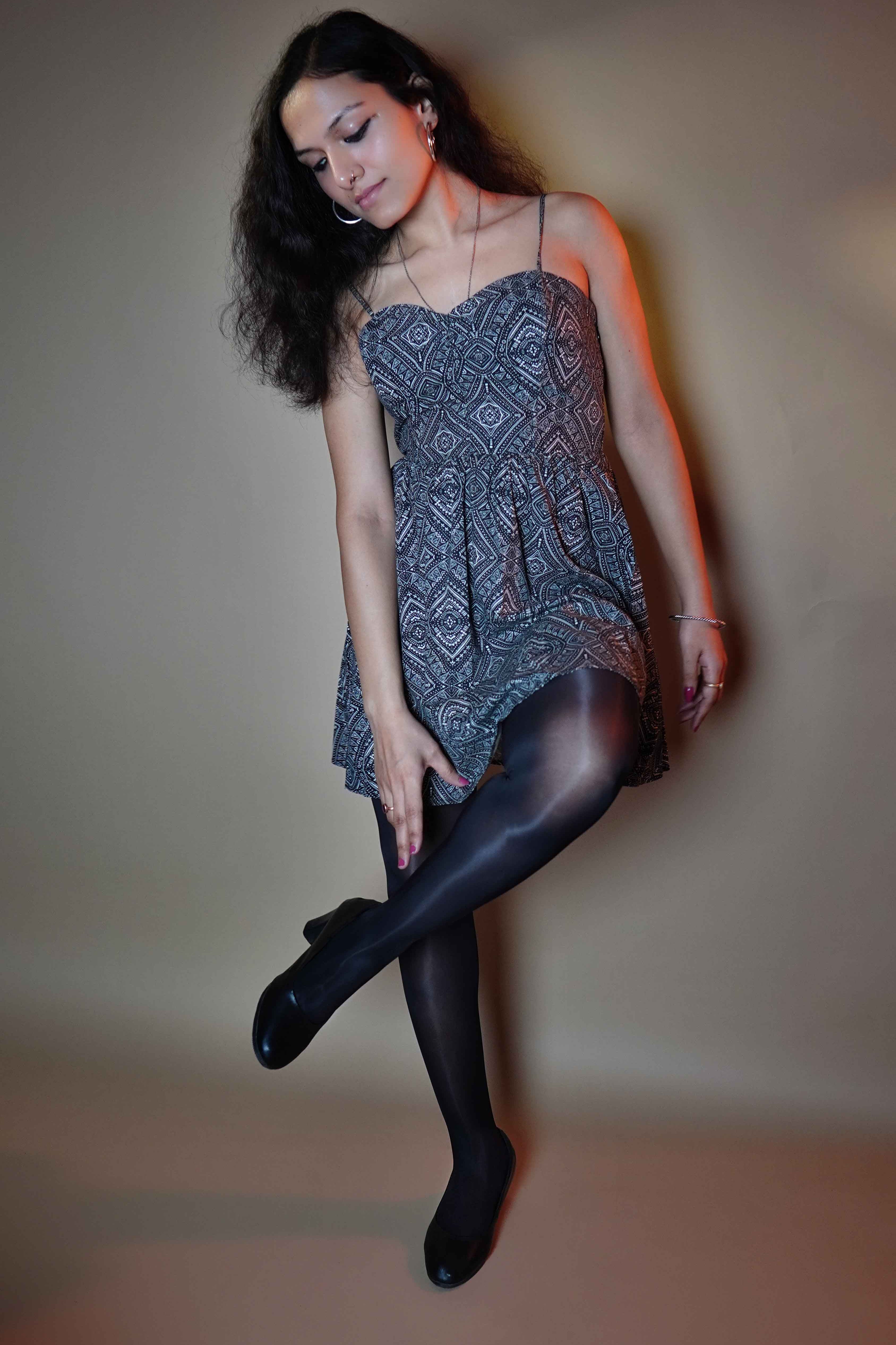 A model wearing women's black stocking posing with her hand reaching to touch her ankle as she pulls up her leg to her knee, slightly bending, highlighting the trendy classy look-Muselot