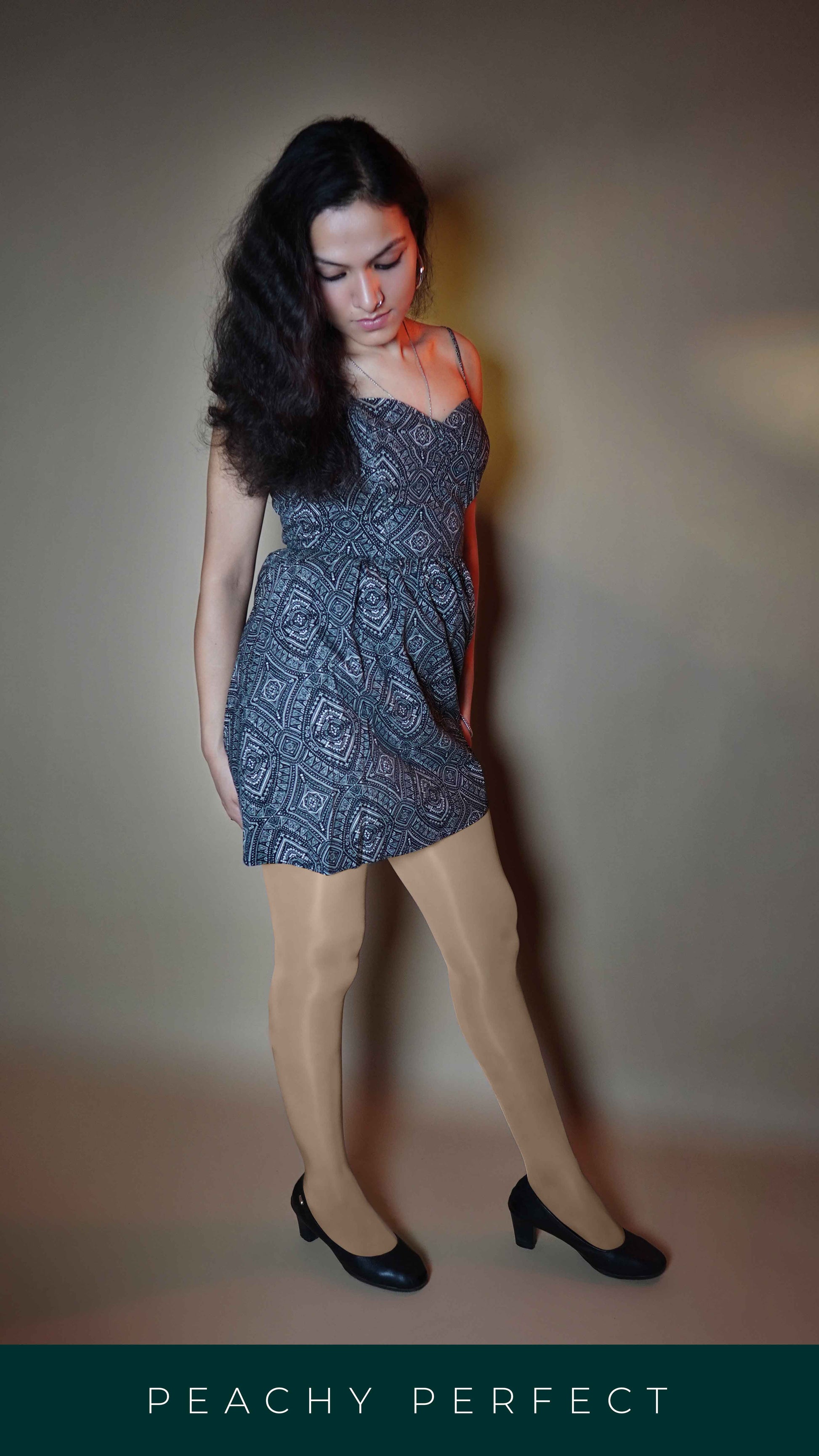 A woman wearing a skin tone premium silky pantyhose, posing with her head bent down slightly and her hands at her back, highlighting a sassy fashionable look-Muselot