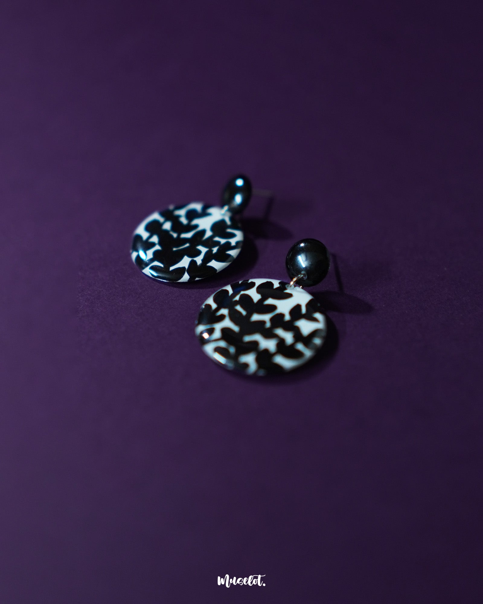 Siyahgul black floral stud earrings, framed by a rich purple backdrop, featuring delicate floral textures and a bold black hue that lend a touch of moody elegance and refined charm — Muselot.