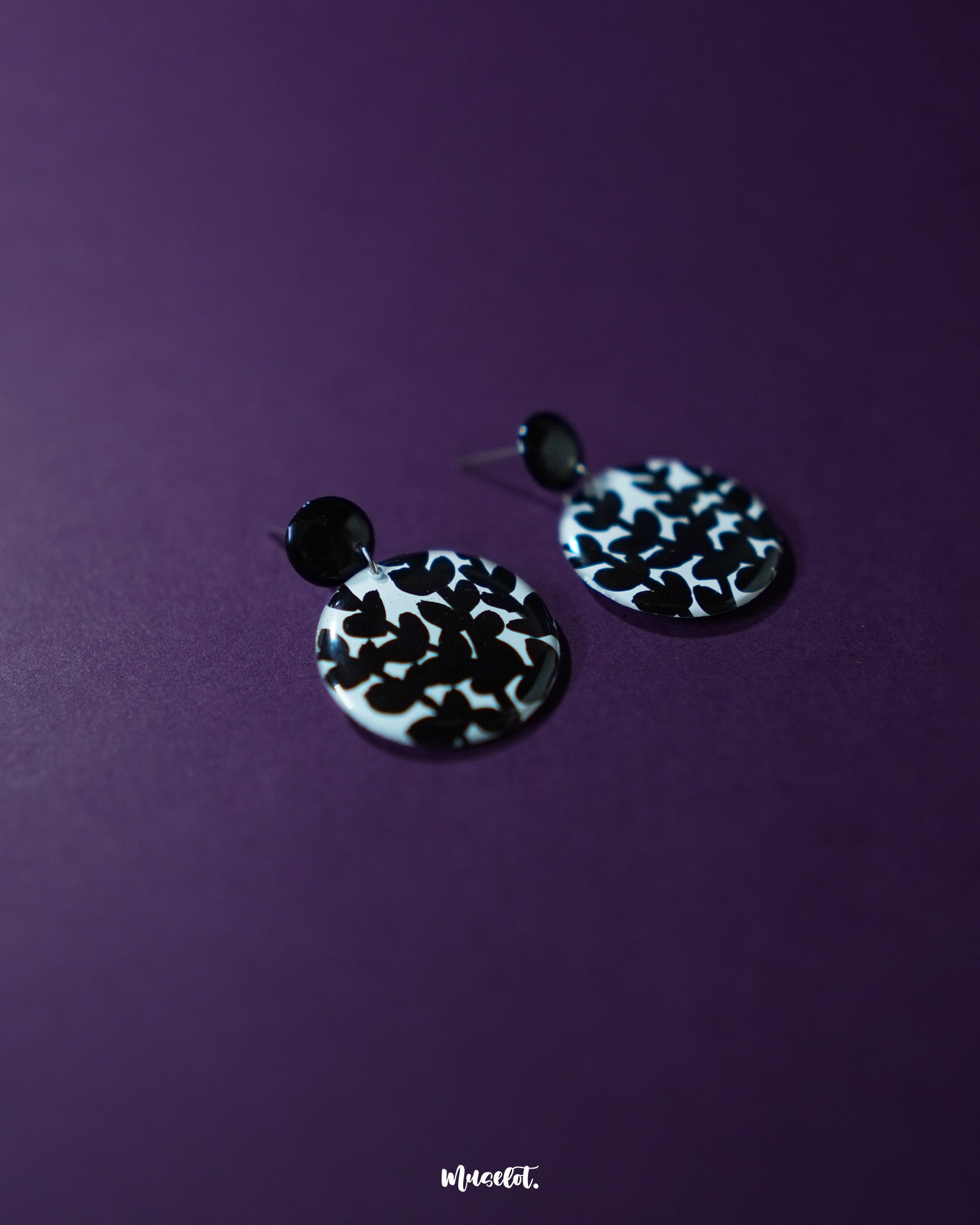 Siyahgul black floral stud earrings, set against a deep purple background, with finely crafted floral details and a striking black tone that evoke a sense of bold, artistic elegance — Muselot.