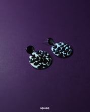 Siyahgul black floral stud earrings, set against a deep purple background, with finely crafted floral details and a striking black tone that evoke a sense of bold, artistic elegance — Muselot.