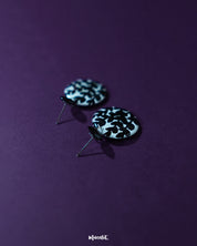 Siyahgul black floral stud earrings, highlighted against a rich purple background, with delicate floral detailing and a deep black hue that bring out their striking elegance and bold charm — Muselot.