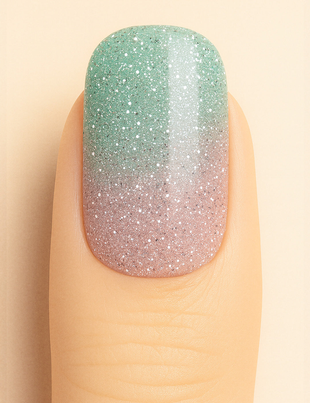 A close-up shot of a model’s finger wearing Snow Petal Ombre Nail Stickies, showcasing a delicate gradient design that blends soft blush pink into a minty green with sparkling silver glitter accents, highlighting the subtle shimmer and smooth ombre transition for an elegant winter-inspired nail art finish – Muselot.