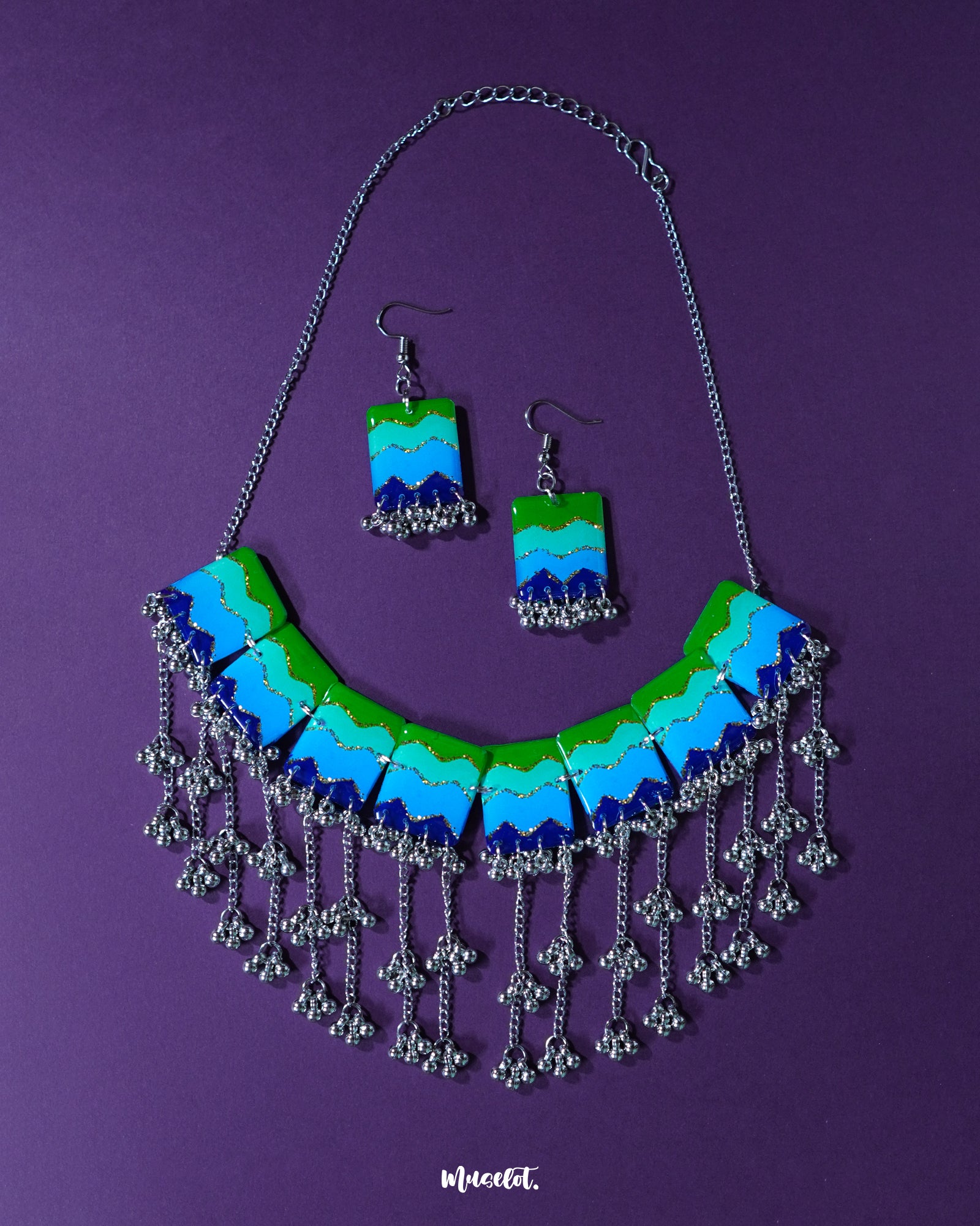 A flat lay of the Sukoon waterfall boho jewelry set displayed on a rich purple background, highlighting its cascading design of multicolored floral elements and metallic charms that evoke a free-spirited, handcrafted elegance — Muselot
