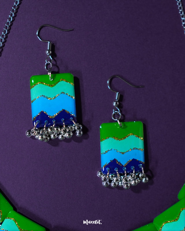 A pair of earrings from the Sukoon waterfall boho jewelry set, designed with silver-toned chains and colorful enamel panels in shades of green and blue. The layered drop style adds movement and charm, making them a standout accessory — Muselot.