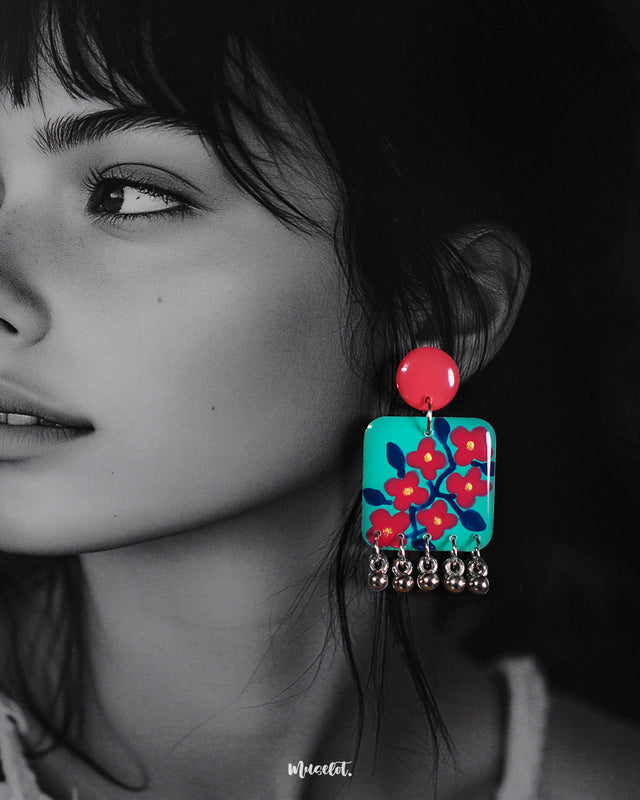 Close-up of a woman wearing the Surkhili floral earrings, highlighting the intricate hand-painted red flowers on a turquoise base and the delicate silver ghungroo drops that add movement and charm — Muselot.