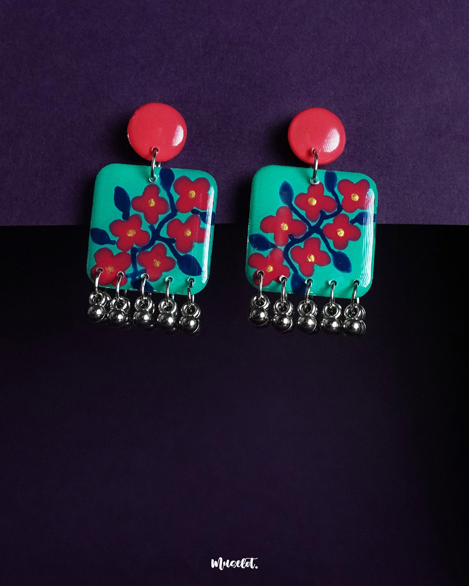 Surkhili floral earrings featuring a vibrant red and turquoise palette with hand-painted red flowers, silver ghungroo danglers, and a glossy red stud top — a bold and artistic statement accessory — Muselot.