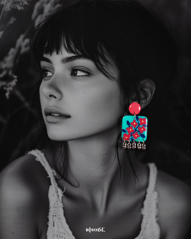 A woman models the Surkhili floral earrings, showcasing their bold turquoise and red design with hand-painted floral details and silver ghungroo accents, adding a vibrant pop of color to her look — Muselot.