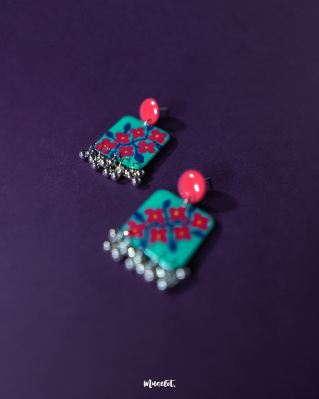 Surkhili floral earrings displayed on a textured backdrop, showcasing their vivid red floral design and silver-toned danglers that lend a festive, handcrafted elegance — Muselot.