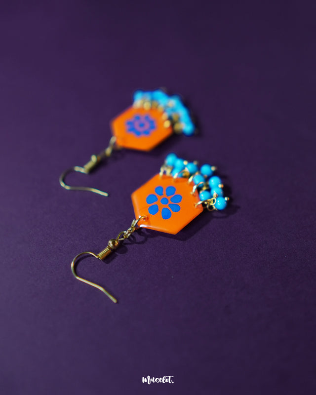 Surkhshaam orange floral stud drop earrings, set against a deep purple background, featuring vibrant blue floral accents and a graceful drop design that add a bold yet refined touch to the look — Muselot.