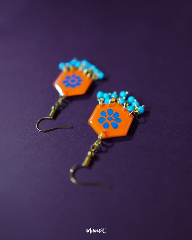 Surkhshaam orange floral stud drop earrings, highlighted against a rich purple backdrop, with vivid blue floral details and a delicate drop that bring out their bold elegance and boho charm — Muselot.