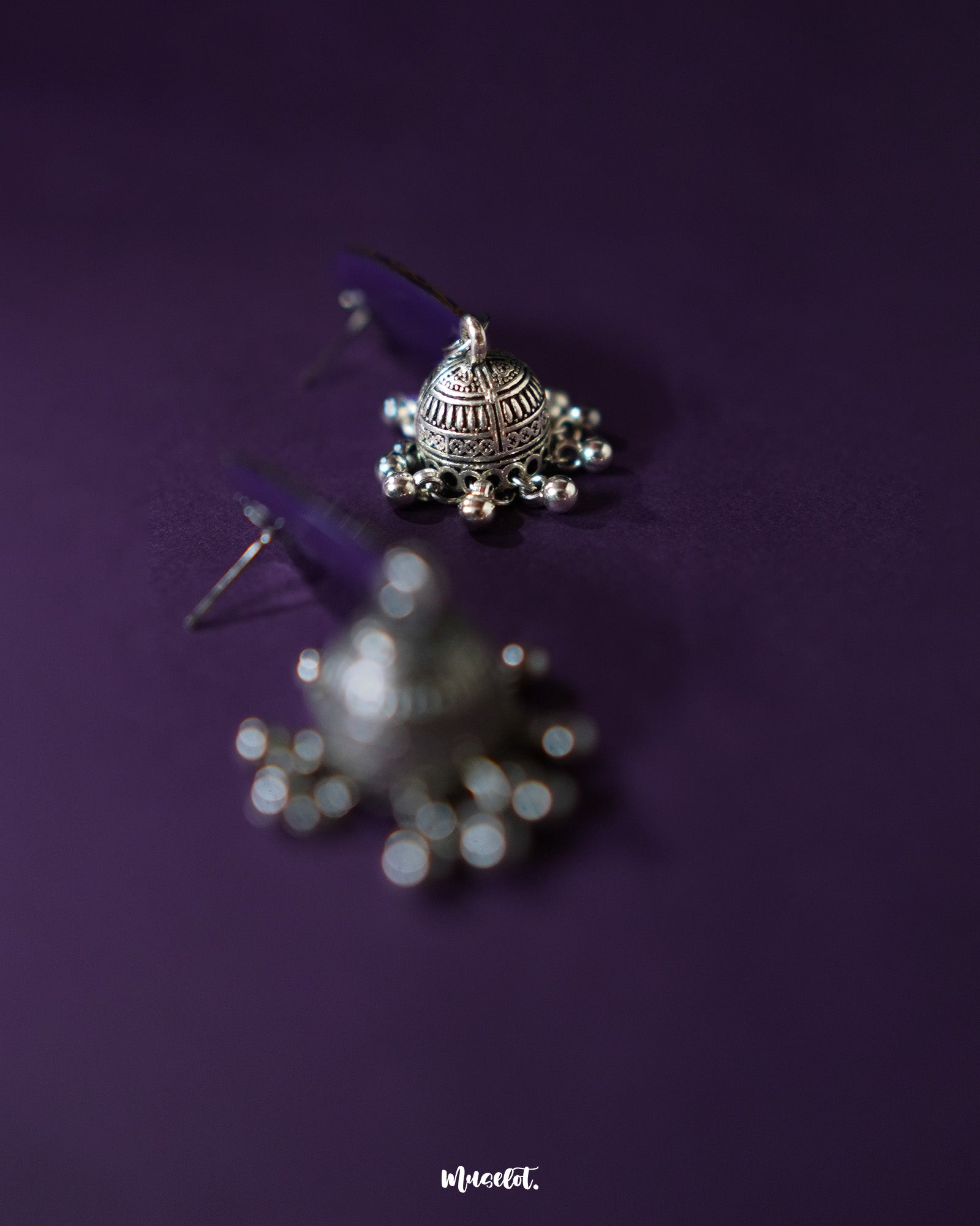 The Tabeer blue jhumkas feature a graceful floral dome design, set against a purple background, highlighting their intricate detailing and timeless elegance — Muselot.