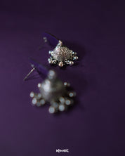 The Tabeer blue jhumkas feature a graceful floral dome design, set against a purple background, highlighting their intricate detailing and timeless elegance — Muselot.