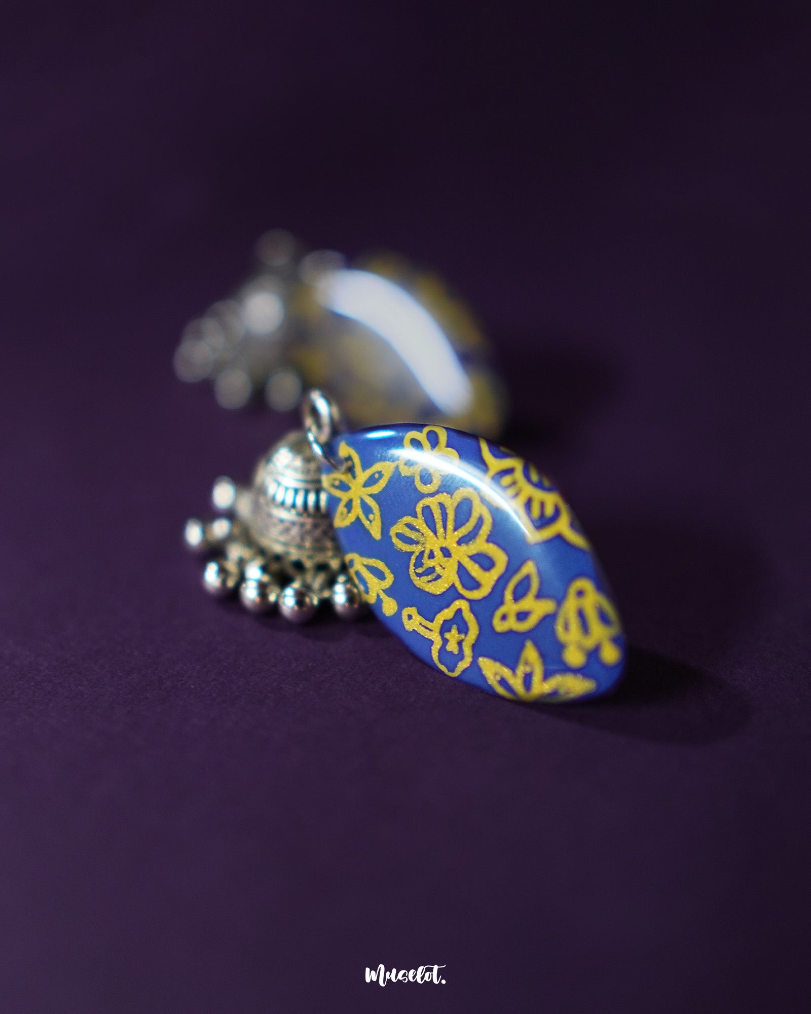 Elegant Tabeer blue jhumkas, adorned with fine floral detailing, stand out beautifully against a soft purple background, showcasing their traditional charm with a modern touch — Muselot.