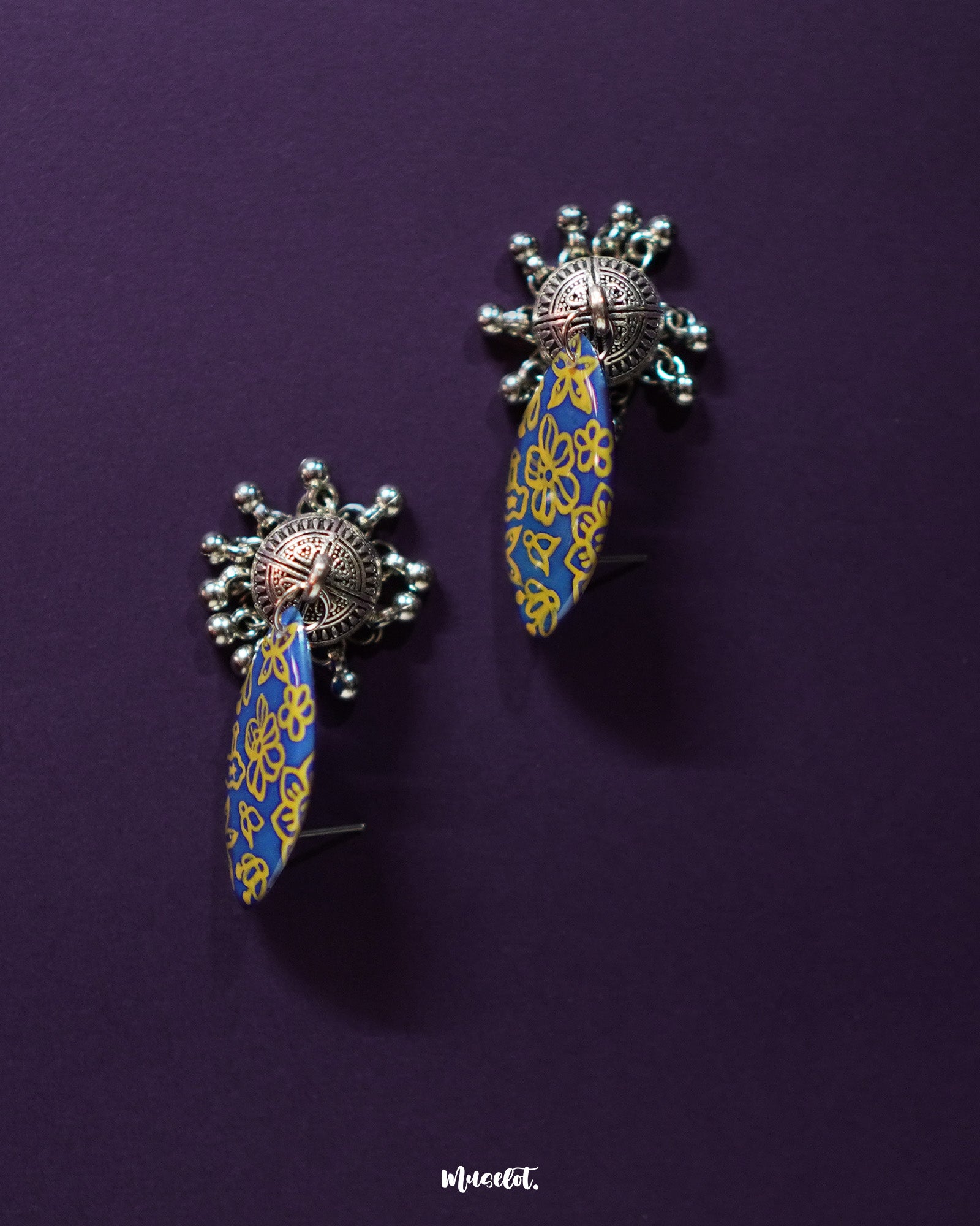 Tabeer blue jhumkas gracefully placed against a dark, contrasting background, emphasizing the detailed floral patterns and exquisite craftsmanship that add a touch of classic sophistication — Muselot.