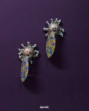 Tabeer blue jhumkas gracefully placed against a dark, contrasting background, emphasizing the detailed floral patterns and exquisite craftsmanship that add a touch of classic sophistication — Muselot.