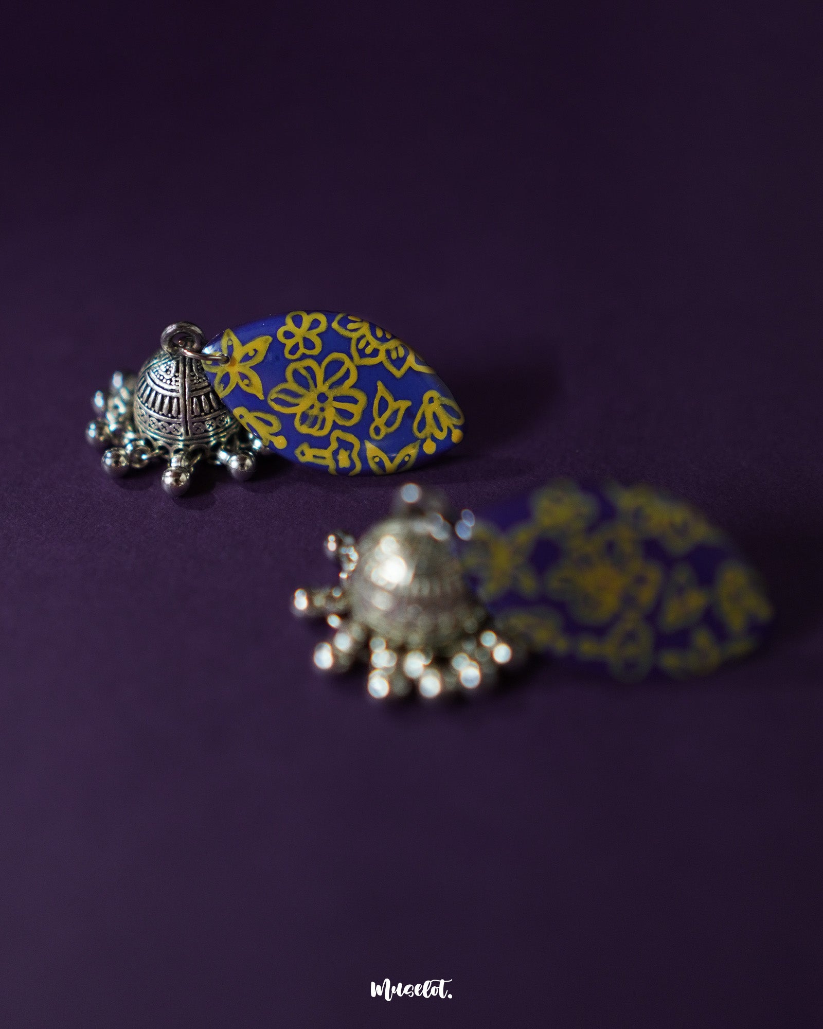 Tabeer blue jhumkas delicately showcased against a dark, contrasting background, with intricate floral patterns and precise detailing that highlight their timeless beauty and elegance — Muselot.