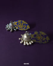 Tabeer blue jhumkas delicately showcased against a dark, contrasting background, with intricate floral patterns and precise detailing that highlight their timeless beauty and elegance — Muselot.