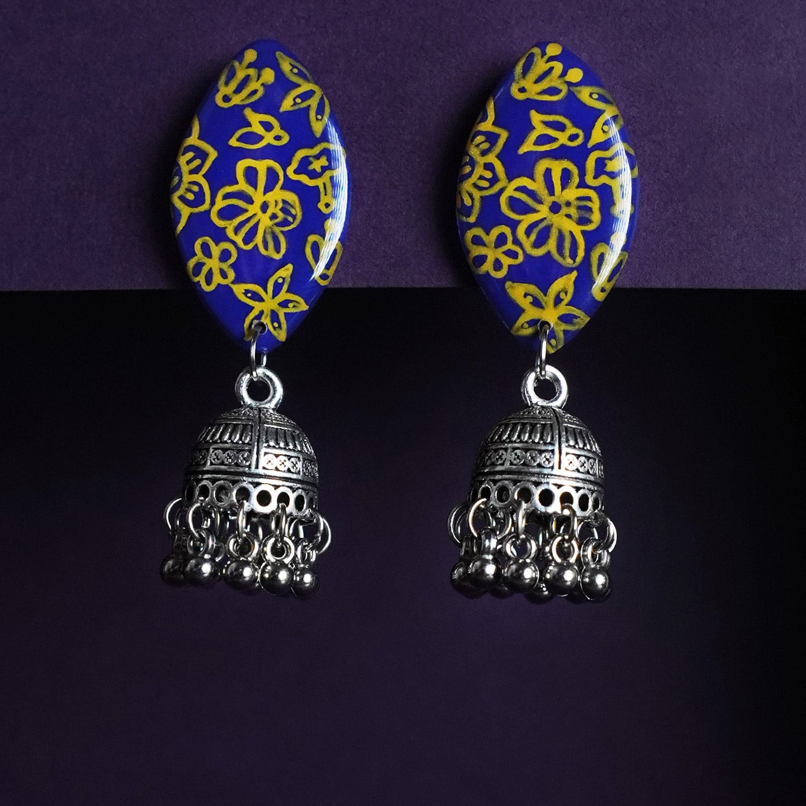 A pair of Tabeer floral jhumkas beautifully displayed against a rich backdrop, highlighting their intricate floral domes and delicate dangling elements. The finely detailed craftsmanship adds an air of timeless elegance, making these jhumkas a perfect choice for festive or traditional wear — Muselot.