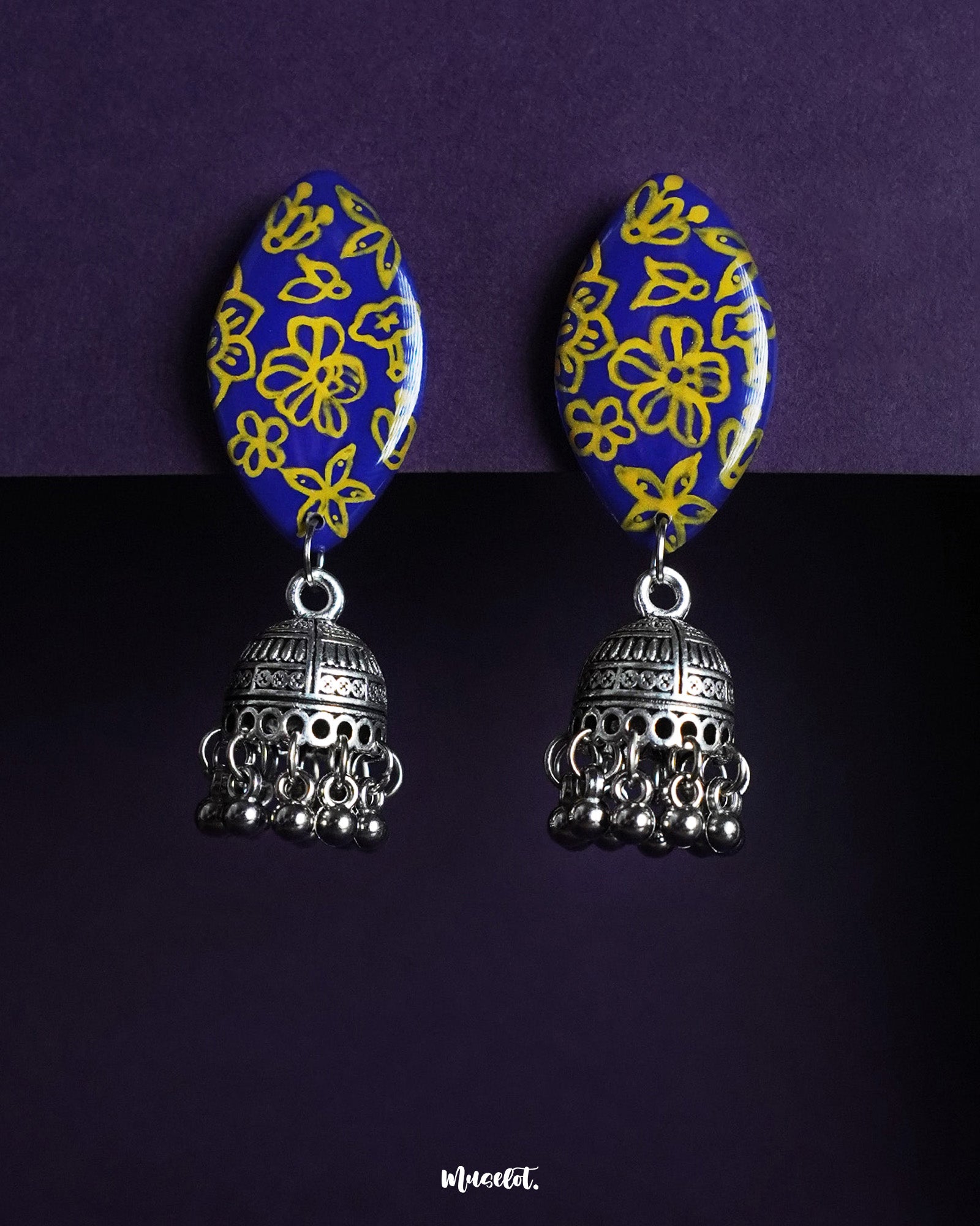 A pair of Tabeer floral jhumkas beautifully displayed against a rich backdrop, highlighting their intricate floral domes and delicate dangling elements. The finely detailed craftsmanship adds an air of timeless elegance, making these jhumkas a perfect choice for festive or traditional wear — Muselot.