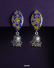 A pair of Tabeer floral jhumkas beautifully displayed against a rich backdrop, highlighting their intricate floral domes and delicate dangling elements. The finely detailed craftsmanship adds an air of timeless elegance, making these jhumkas a perfect choice for festive or traditional wear — Muselot.