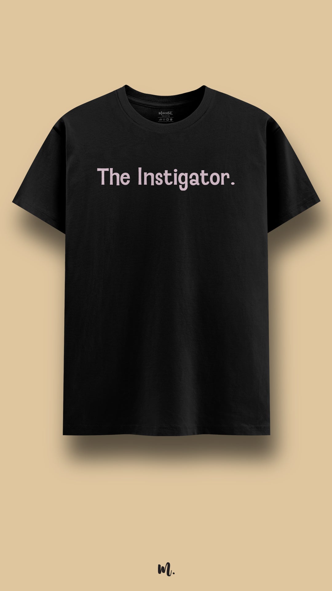 Black graphic t-shirt showcasing the statement “The Instigator.” in soft pink typography, highlighting a bold, playful, and slightly mischievous personality against a clean beige background – Muselot