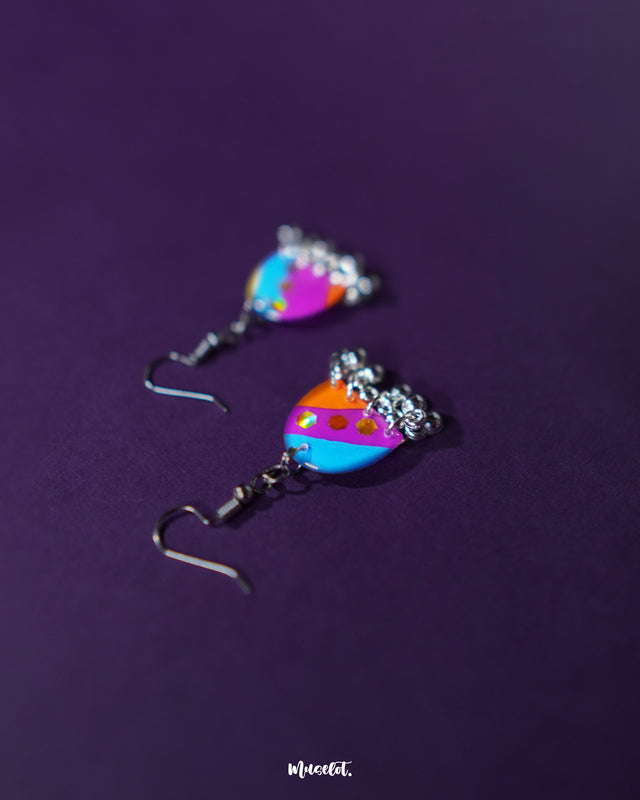 Ufaq multicolor hook earrings, set against a rich purple background, with vibrant colors and geometric patterns that bring out the earrings' bold yet refined elegance — Muselot.