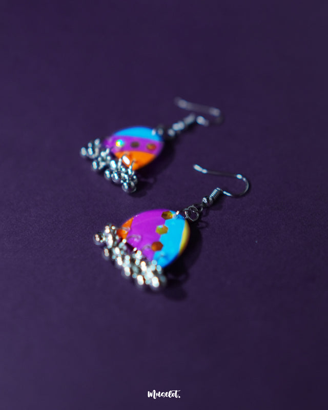 Ufaq multicolor hook earrings, elegantly framed by a rich purple background, with a vibrant array of colors and distinctive geometric patterns that highlight their eye-catching and refined style — Muselot.