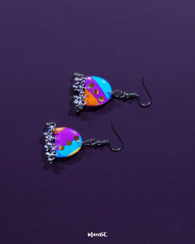 Ufaq multicolor hook earrings, set against a deep purple backdrop, with striking colors and bold patterns that accentuate their unique and sophisticated design — Muselot.