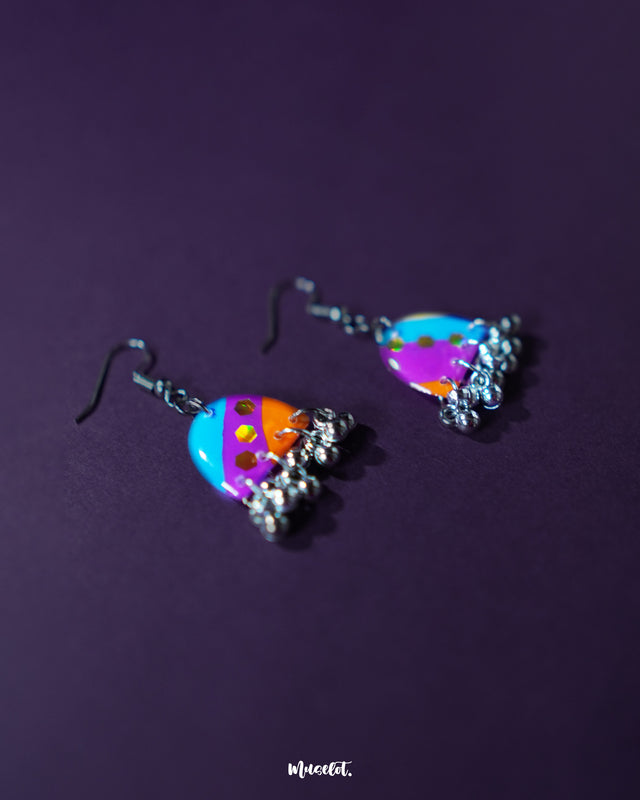 Ufaq multicolor hook earrings, placed against a dark purple background, featuring an explosion of vibrant hues and intricate patterns that enhance their bold yet elegant look — Muselot.