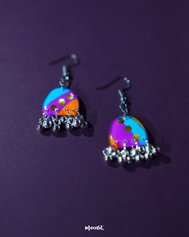 Ufaq multicolor hook earrings, showcased against a rich purple background, with a blend of vibrant colors and geometric designs that highlight their playful and sophisticated charm — Muselot.